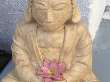 A statue holds a pink lotus flower in its hands.
