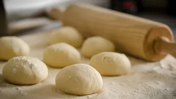 Dough balls on floured surface, rolling pin nearby.