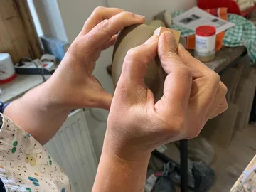 Hands form clay and attach a piece of wood.