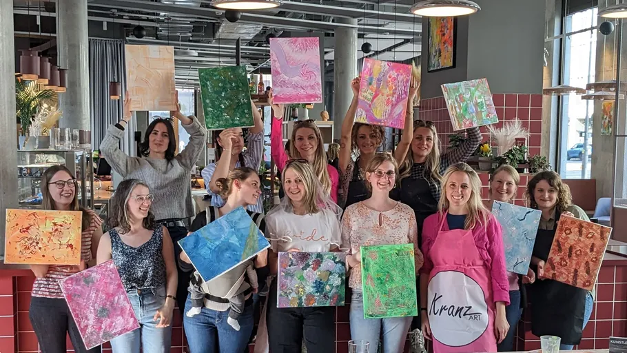 Group of women holding colorful paintings indoors.