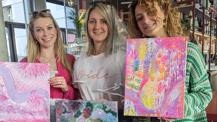 Three women holding colorful paintings indoors.