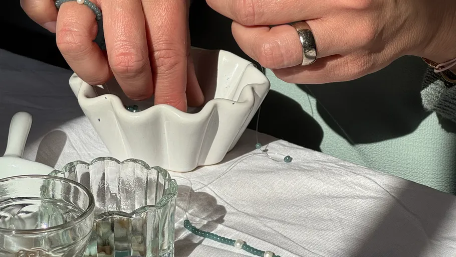 Hände fädeln Perlen über Tisch.