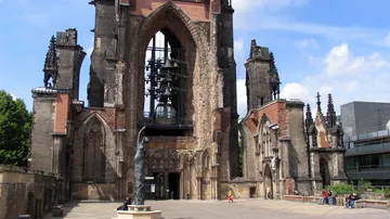 Ruined church with statue and people outside.