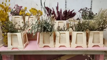 Getrocknete Blumen in Plastikkisten auf Regal.