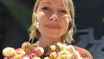Person lächelt, hält bunte Blumen, sonniger Tag.