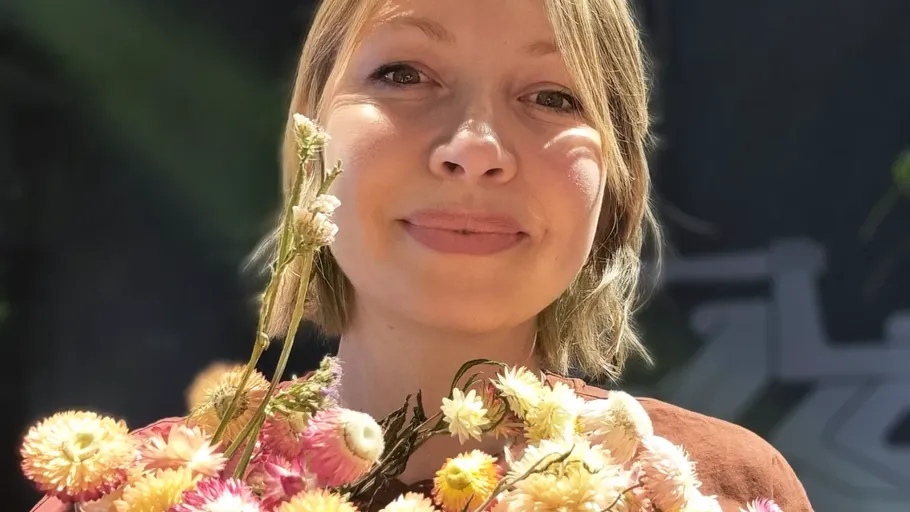 Person lächelt, hält bunte Blumen, sonniger Tag.