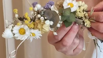 Hände halten ein Blumen-Haarband drinnen.
