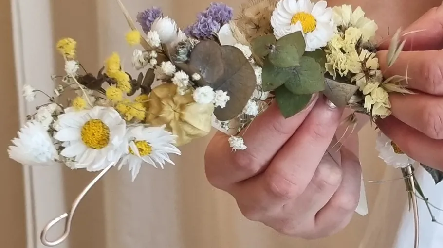 Hands holding a floral headpiece indoors.