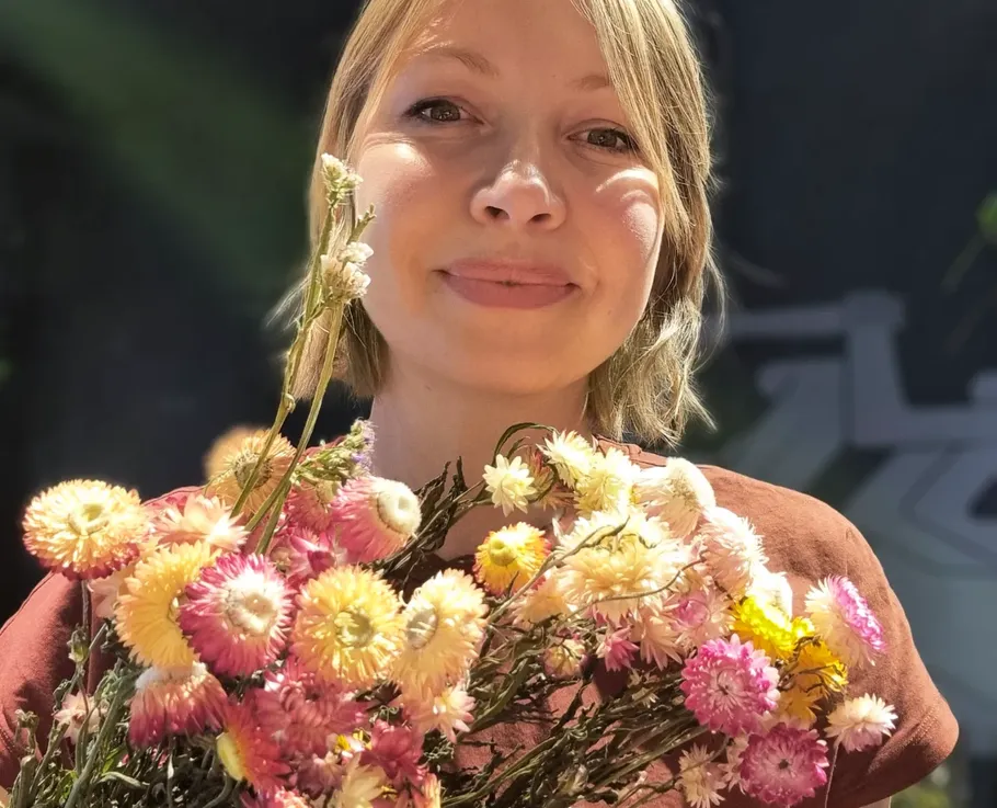 Person smiling, holding colorful flowers outdoors.