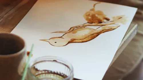 Vogelmalerei auf Papier neben Tasse.