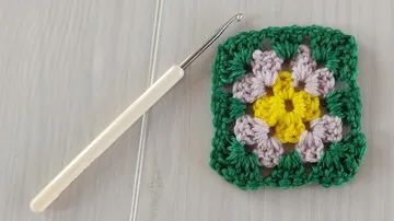 Häkelnadel neben einem bunten Granny Square.