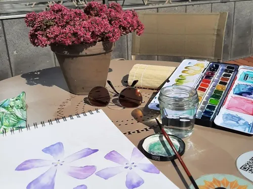 Aquarellpalette, Pinsel malt Blumenzeichnung am Tisch draußen.