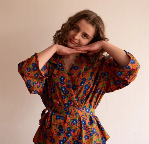 Woman posing in floral dress, neutral background.