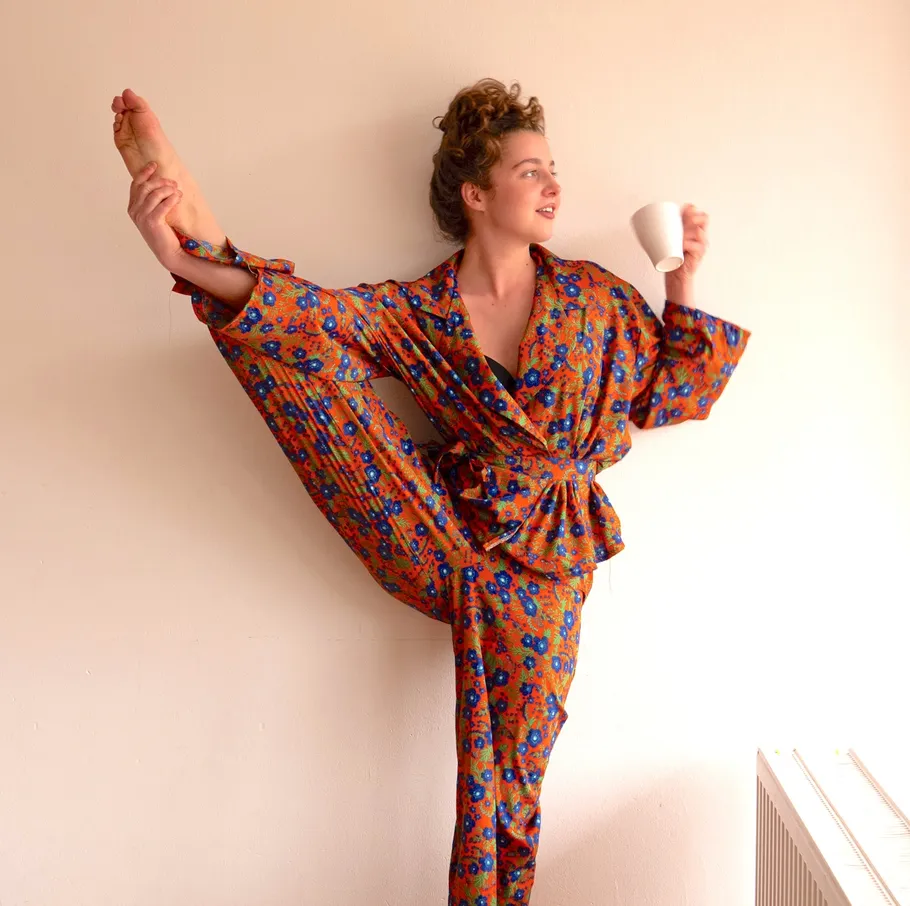 Person in pajamas doing yoga, holding mug.