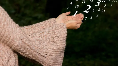 Hands in sweater holding floating numbers outdoors.