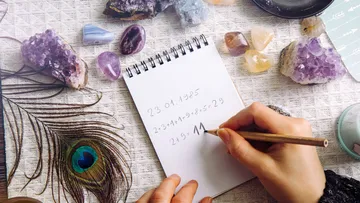 Hands writing on notepad surrounded by crystals.