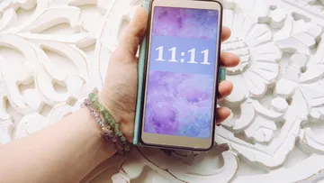 Hand holds smartphone displaying 11:11 on screen.