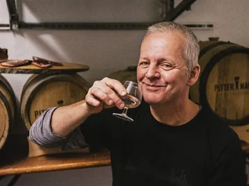 Man raises glass, smiles in a wine press.