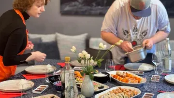 Two people preparing a table with sushi.