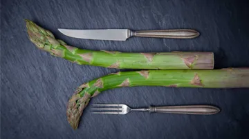Asparagus and cutlery on dark slate.