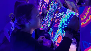 Person painting vibrant artwork under blacklight.