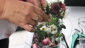 Hände arrangieren Blumen auf einem Tisch.