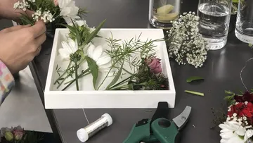 Hände arrangieren Blumen auf einem Tisch.