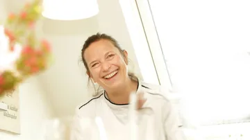 Smiling woman sitting in bright kitchen.