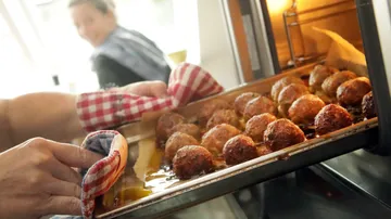 Meatballs being taken out of oven.