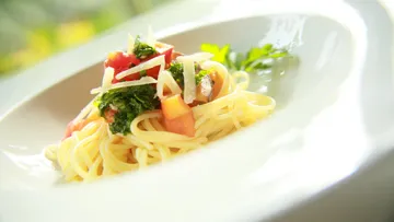 Pasta mit Tomate, Kräutern und Käse auf Teller.