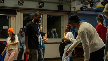 Menschen tanzen energisch in einem dämmerigen Studio.
