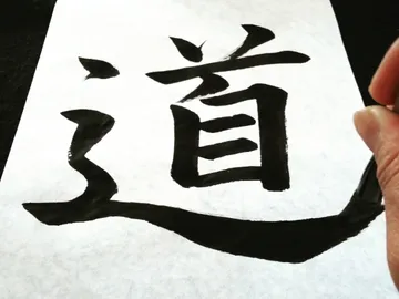 Ein Pinsel schreibt chinesische Schriftzeichen auf Papier.