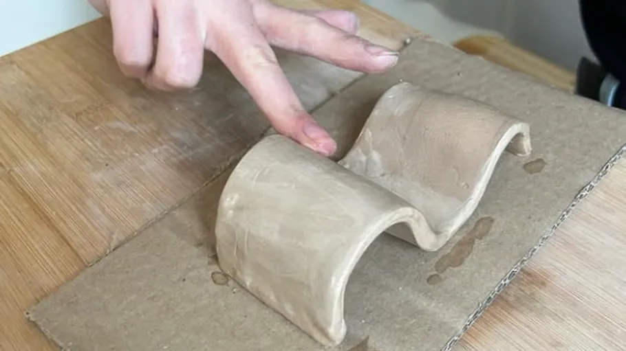 Clay sculpture being shaped by hands on cardboard.