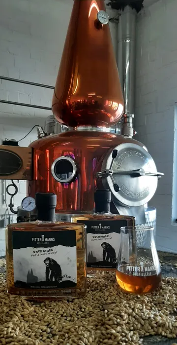 Whiskyflaschen auf Getreide, Brennerei im Hintergrund.