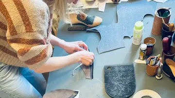 Person crafting leather shoes on table.