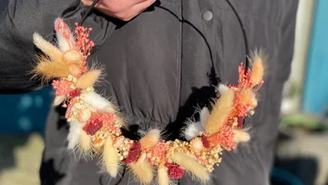 Hand hält bunten Trockenblumenkranz im Freien.
