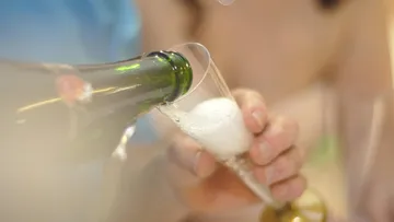 Hand gießt Champagner in ein Sektglas.