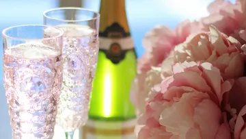 Gläser und Blumen nahe Sektflasche.