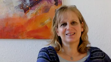 Smiling woman seated near colorful painting.