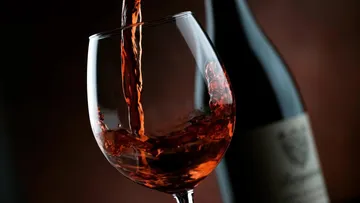 Red wine pouring into a glass, dark background.