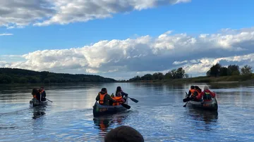 Menschen paddeln auf ruhigem Fluss unter blauem Himmel.