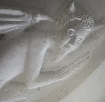 Steinschnitzerei einer gehörnten Figur im Relief.