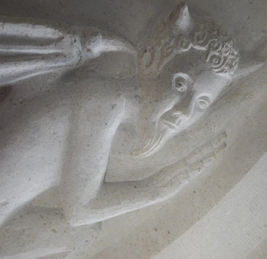 Steinschnitzerei einer gehörnten Figur im Relief.
