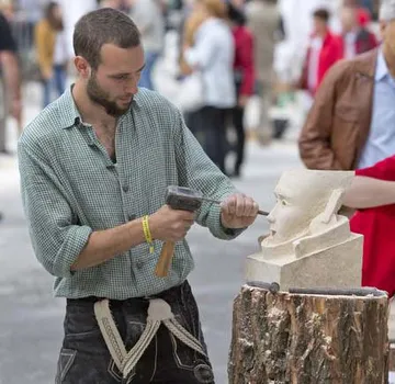 Mann meißelt Steinskulptur im Freien.