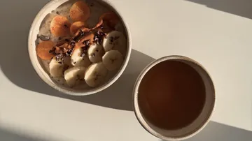 Frühstücksschüssel mit Obst neben Kaffee.