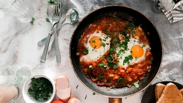 Shakshuka kocht in einer Pfanne auf Tisch.