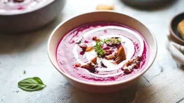 Lila Suppe mit Kräutern und Sahnewirbel garniert.