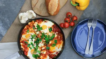 Shakshuka in Pfanne mit Brot und Gemüse.