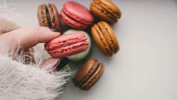Hand holding a pink macaron with various others.