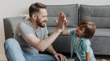 Vater und Sohn geben High-Five auf Wohnzimmerboden.
